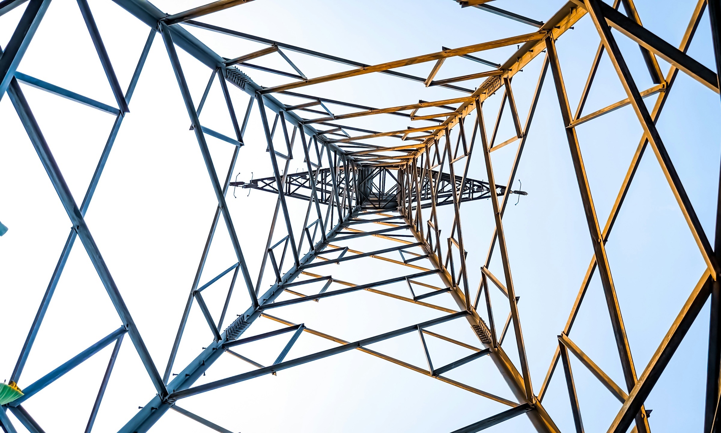 Low-angle view of a steel transmission tower against a clear blue sky.
