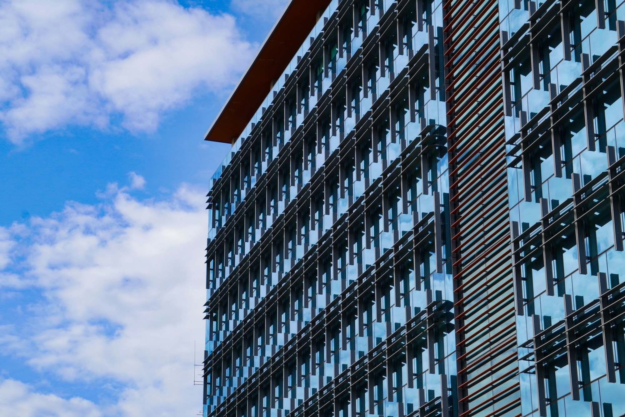 Modern glass office building with reflective windows under a blue sky with scattered clouds.